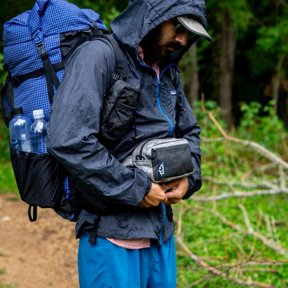 Hiker adjusts water-resistant ULTRA Spare Tire Waist Pack in Rain