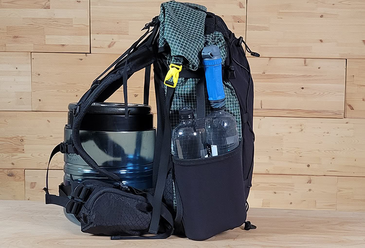 Backpacker reaches for his bear spray from the ULA Deploy Bear Canister Holder on his shoulder strap.